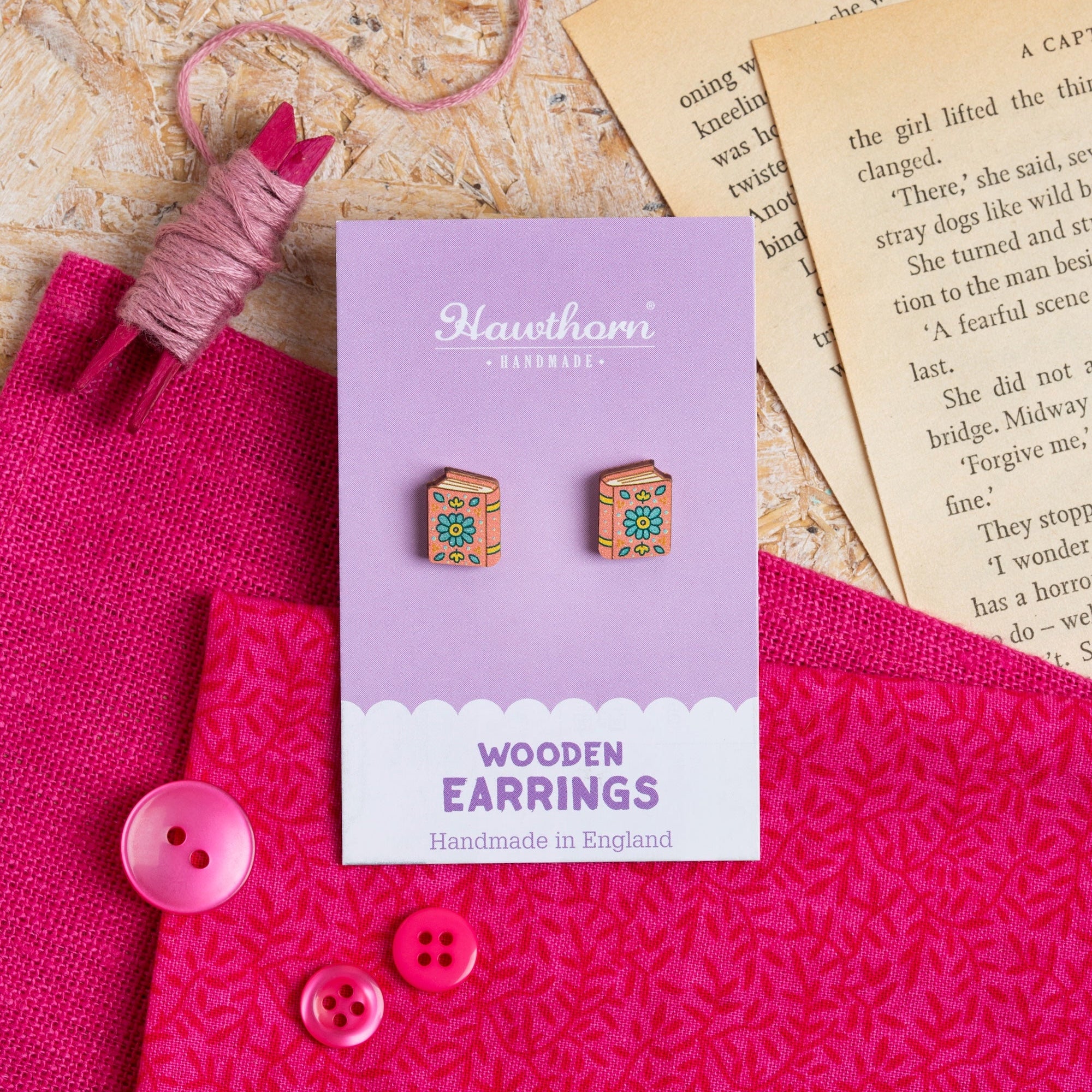 Hawthorn Handmade book Wooden Earrings packaging on a textured surface with pink fabric and buttons.