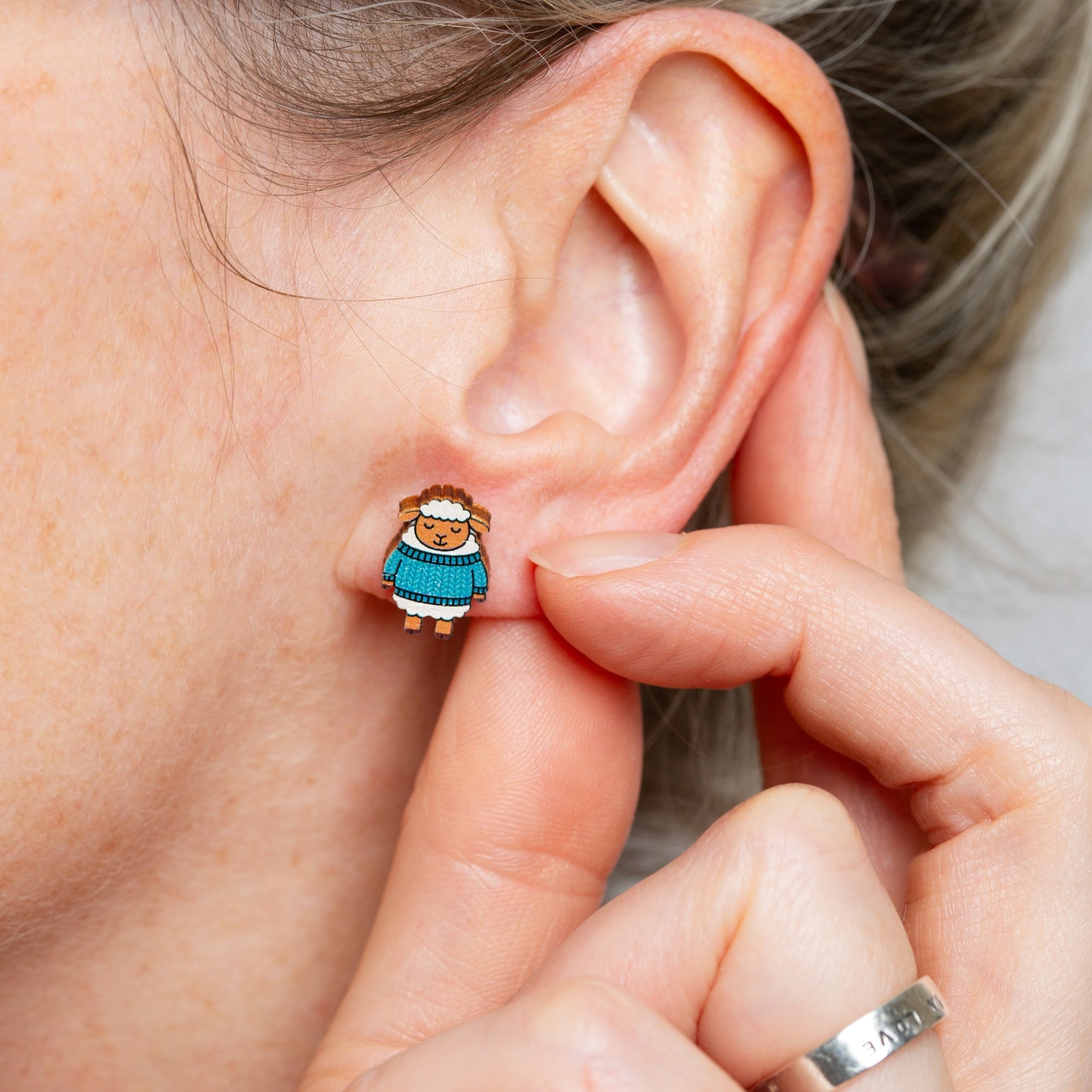 Person wearing a small earring with a character design, held close to the ear.