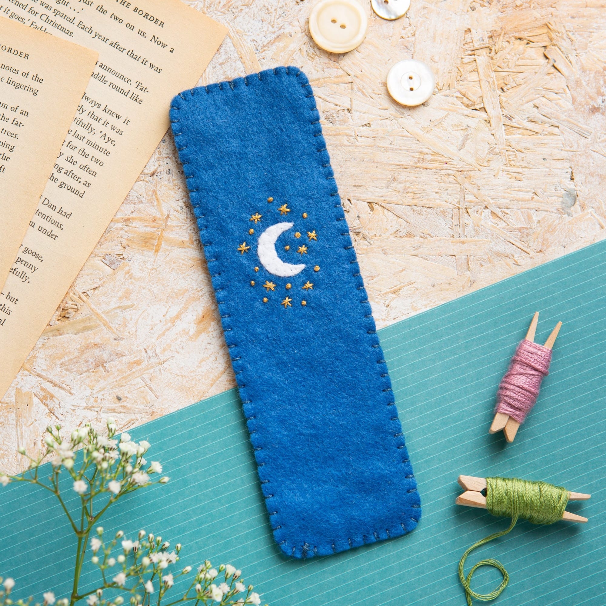 Blue embroidered hare bookmark on a textured surface with buttons and a book.