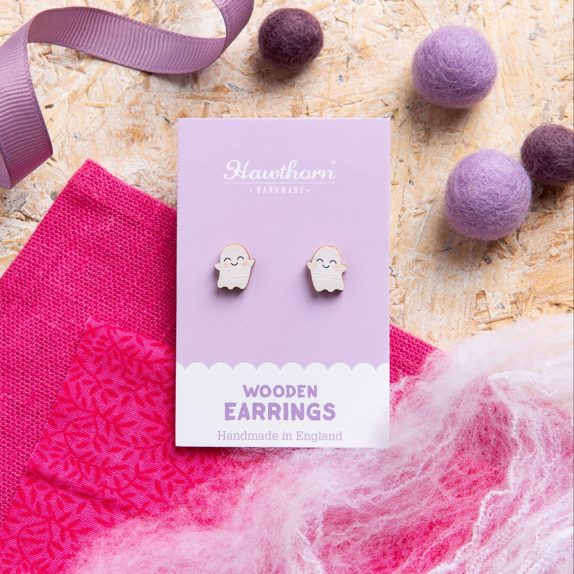 Ghost wooden earrings with pink fabric and purple ribbons on a textured surface