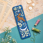 Embroidered bookmark with a hare design on a textured surface with sewing materials.