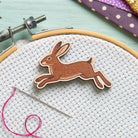 wooden hare design needle minder on embroidery hoop, pink thread, and gold scissors on a polka dot fabric background.