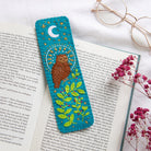Decorative bookmark with an owl design on an open book with glasses and flowers.