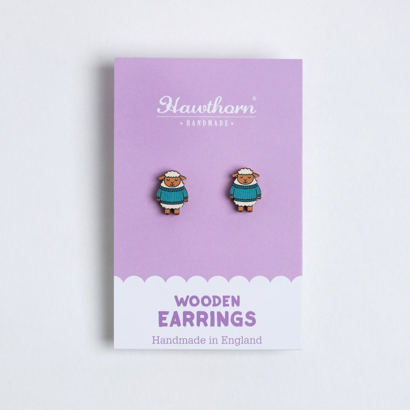 Pair of sheep wooden earrings on a purple card with 'Hawthorn' branding.