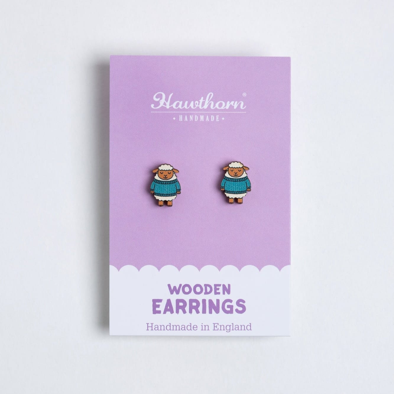 Pair of sheep wooden earrings on a purple card with 'Hawthorn' branding.