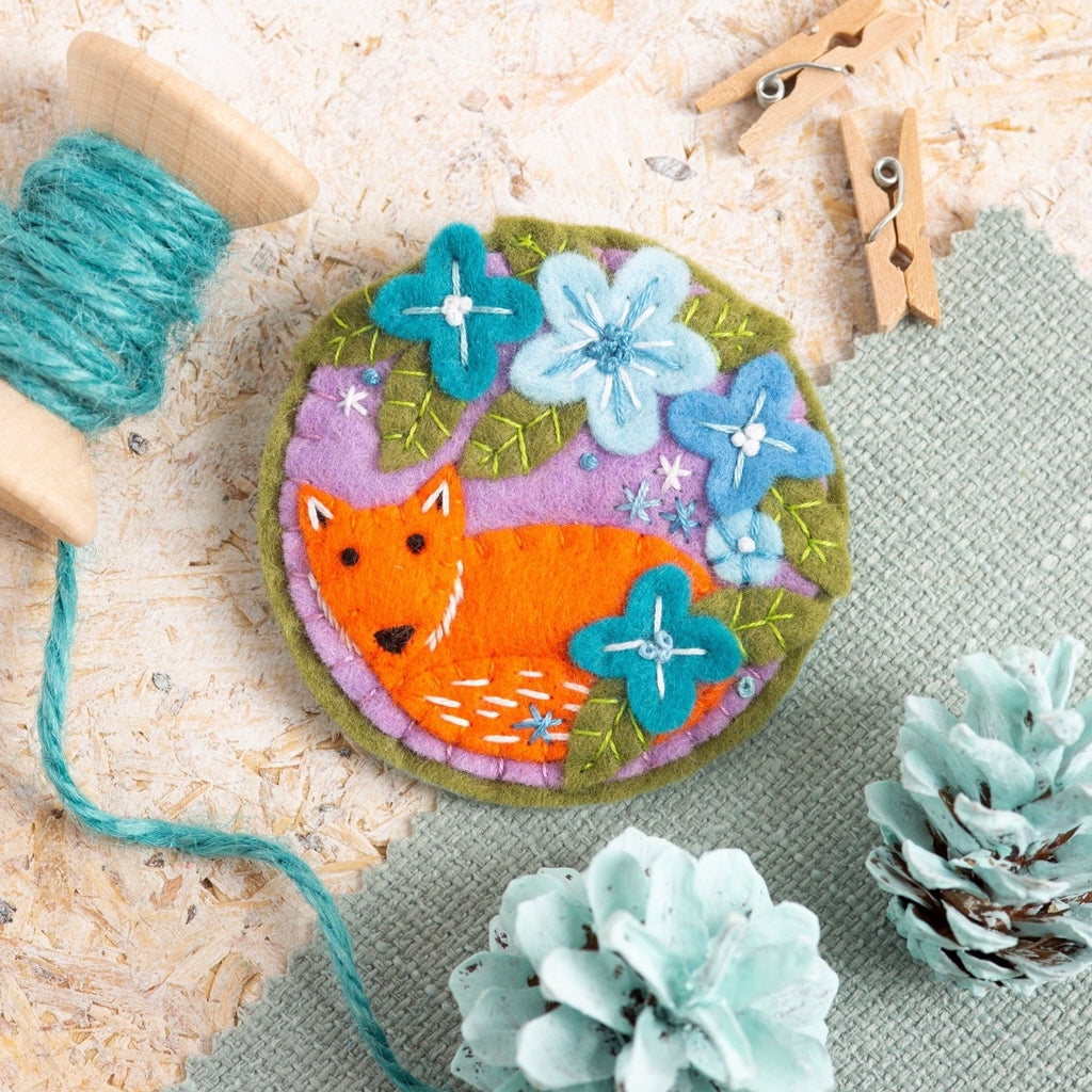 Fox brooch felt craft kit displayed on wooden background with mint green painted pine cones.