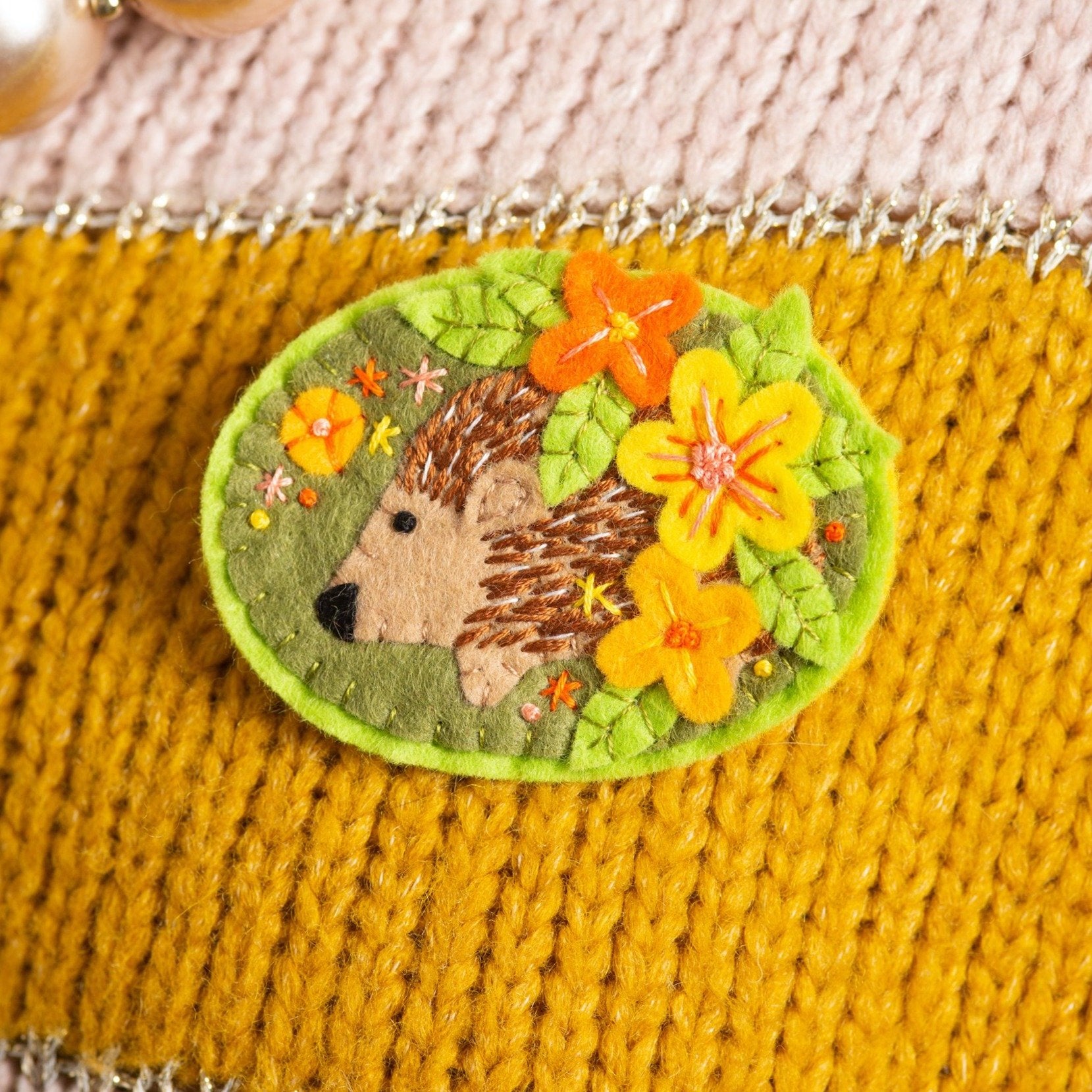 Hedgehog felt brooch worn on mustard and cream coloured knitted jumper