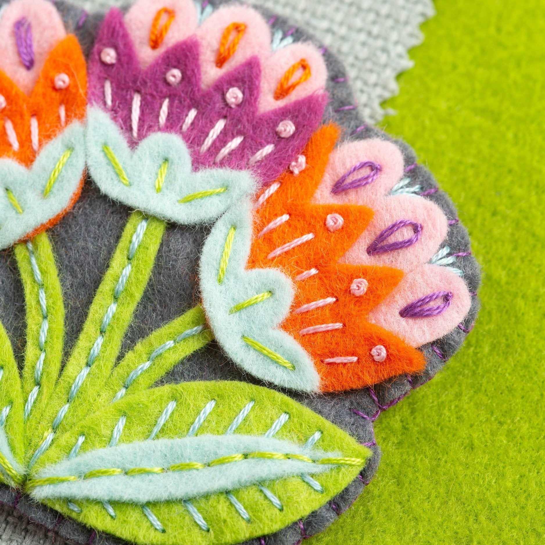 Close up image of Marianne flower brooch on green felt background.
