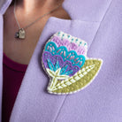 Vita flower brooch worn on lapel of purple coat.