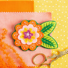 Margery Flower Brooch displayed on orange, yellow and peach background.